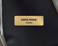 A rectangular gold-toned name badge with a brushed metal-look finish. The text SOFIA ROSSI is engraved in black capital letters, with the word Hostess below in smaller black letters. The badge is centered against a dark background.
