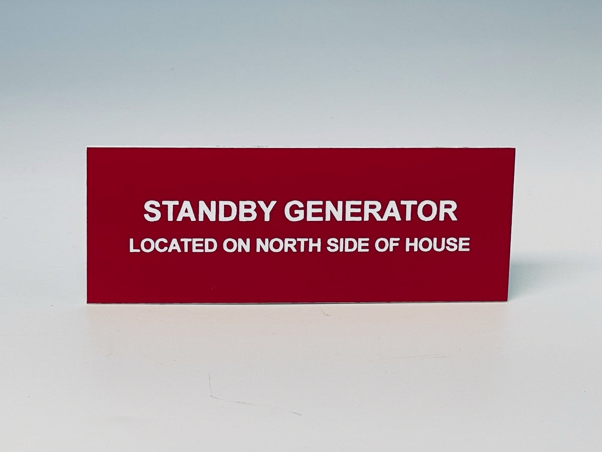 Red engraved label with white letters reading STANDBY GENERATOR, LOCATED ON NORTH SIDE OF HOUSE.