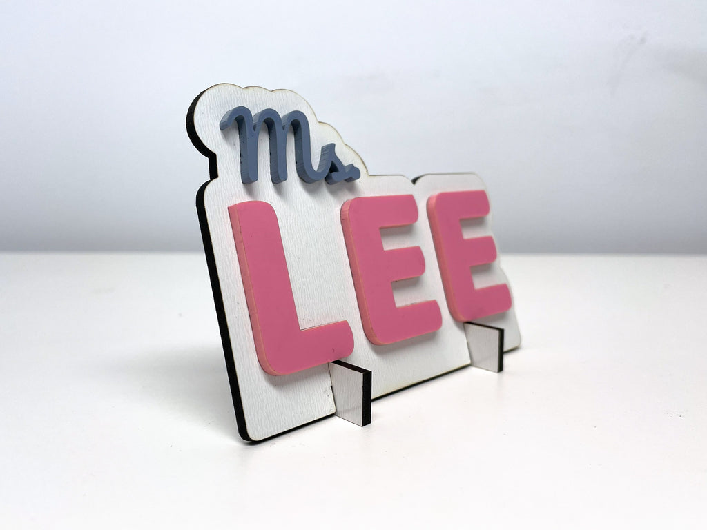 The Ms. LEE teacher sign at an angle, showing the pink letters standing off the white finish base.